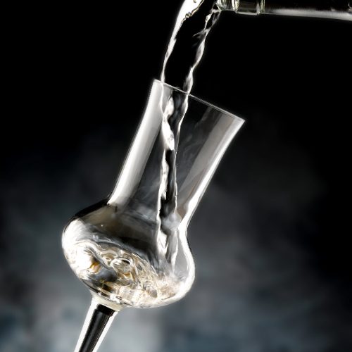 Hauseigene Brennerei Ein Schnaps-Glas wird mit klarem Destillat gefüllt, vor dunklem Hintergrund.